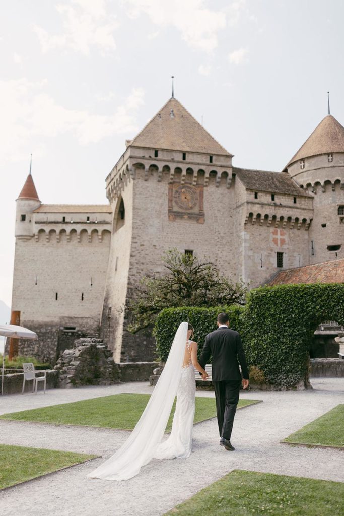 Woman in a wedding dress with a long veil with her husband in front of Château de Chillon in Switzerland during their Swiss destination wedding.