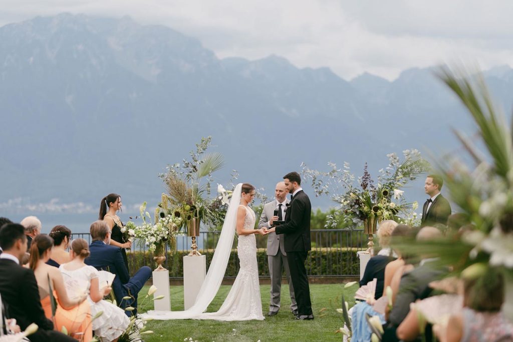 Swiss destination wedding couple exchanges vows at an outdoor lakeside ceremony on the grounds of the Fairmont Montreux Palace.