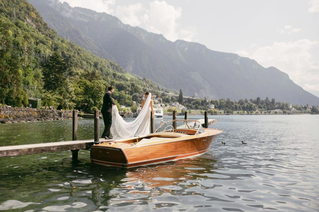 Groom holds bride’s veil as they walk on a dock before boarding a boat on Lake Geneva for a picturesque, romantic boat ride on their wedding day.