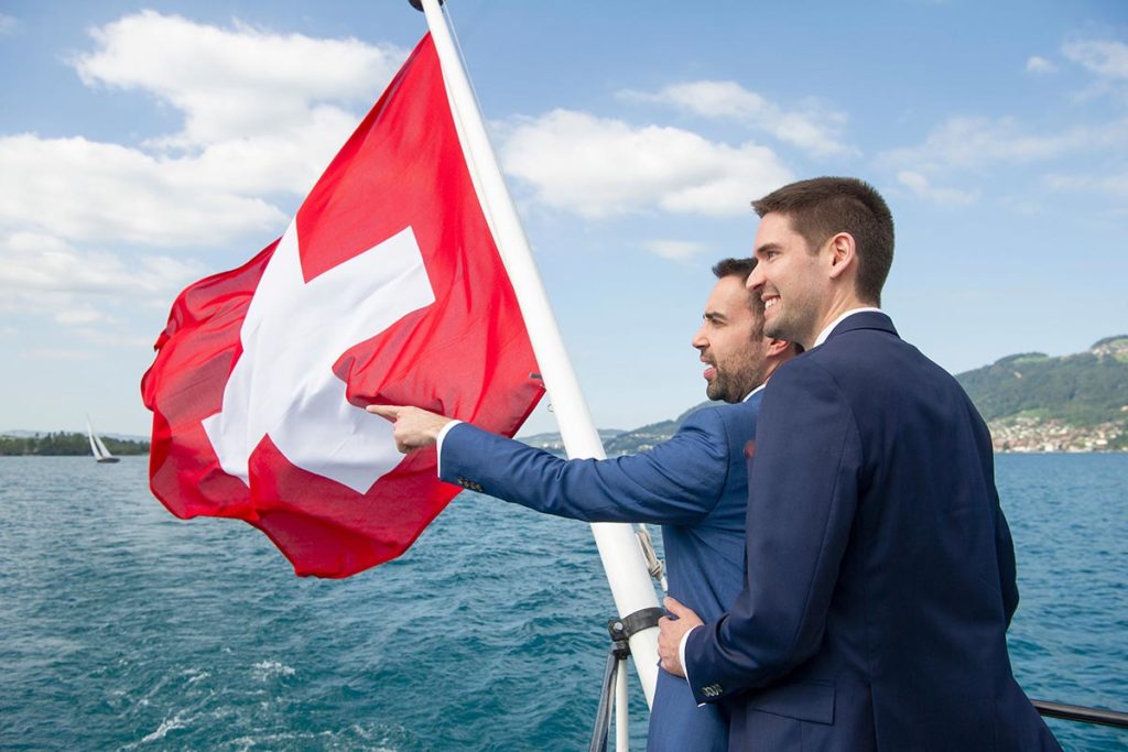  Two men wearing suits on their wedding day while on a boat on Lake Thun, as part of their destination gay wedding in Switzerland.