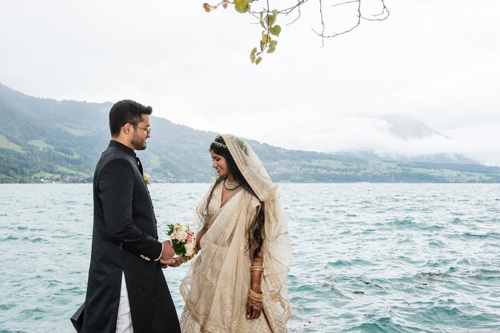 Indian bride and groom stand on the waterfront as they pose for pictures on their wedding day in Switzerland.
