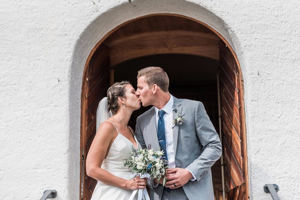 : Bride and groom kiss in front of a door archway in the Sertig Valley, Davos.