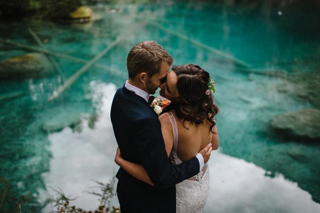 Wedding photo of a couple embracing in front of the turquoise waters of Lake Blausee, part of their small Swiss wedding.