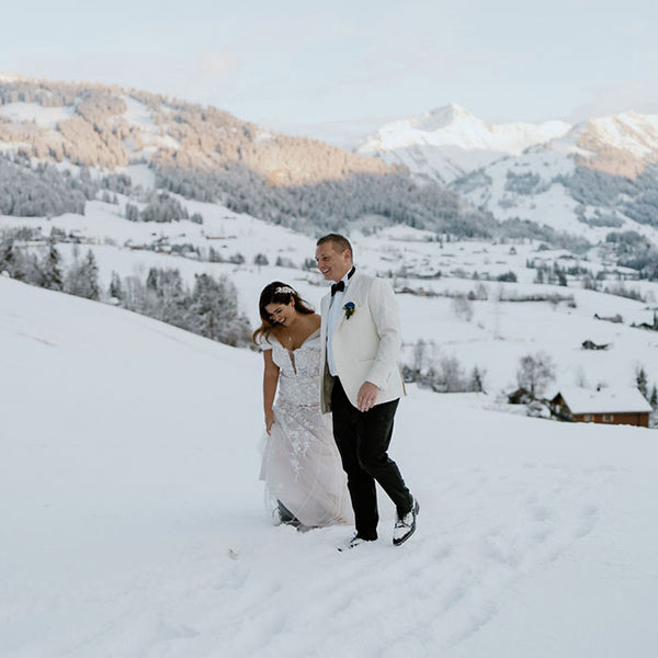 A bride and groom in Black tie dress walk across the snow covered mountain slopes after their wedding celebration at The Huus, Gstaad, Switzerland