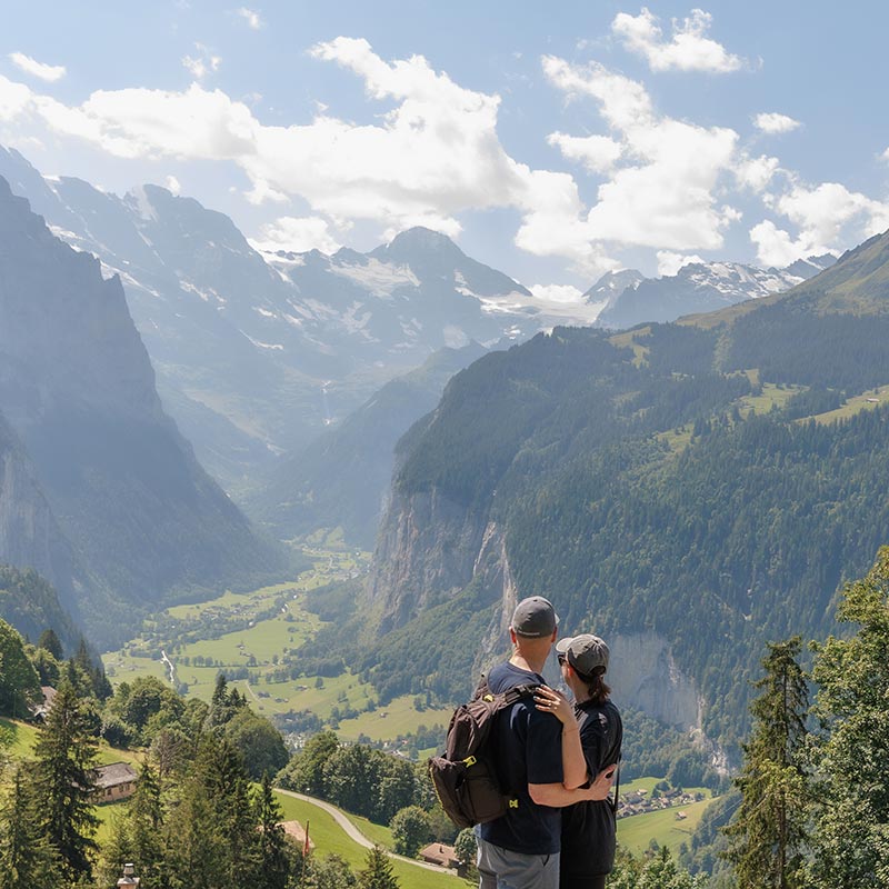 An engaged couple look over the Lauterbrunnen Valley in Switzerland after their Swiss proposal portrait session with Emma Wilson, engagement photographer and videographer