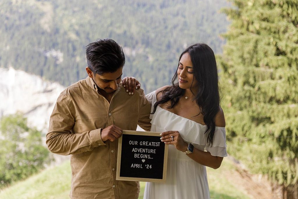 Husband and wife announce that they are pregnant with a sign—photo taken while in Switzerland, on their “babymoon” vacation trip