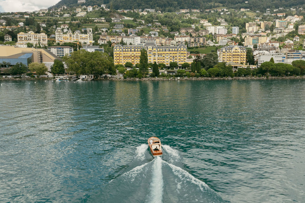 A drone shot of a wedding couple approaching the Montreux Palace in a luxury wooden speedboat on their wedding day